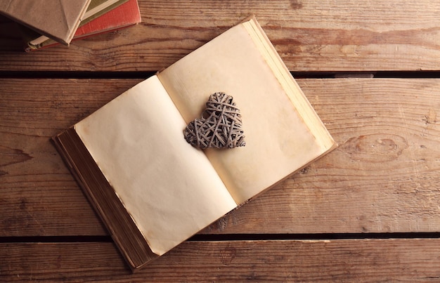 Old open book and decorative heart on wooden background top view