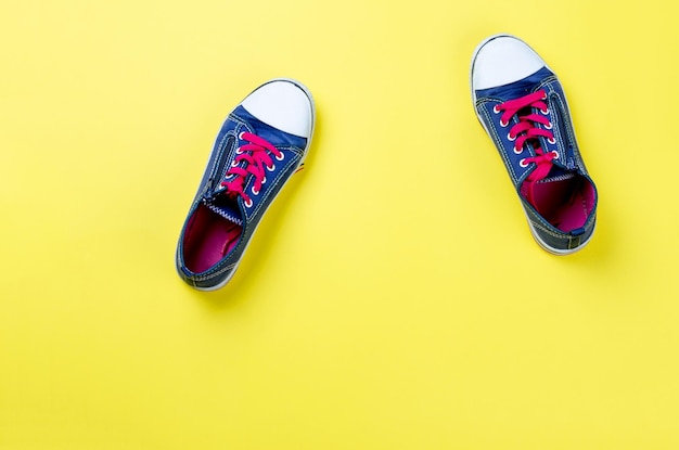 Old pair of blue sneakers on yellow background top view with space for text