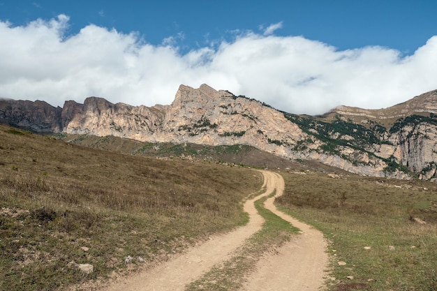 Old path through mountains Trekking mountain trail Bright atmospheric minimalist alpine landscape with stony footpath among grasses in highlands Pathway uphill Way up mountainside