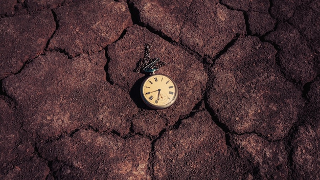 An old pocket watch lies on dry ground. Past and future tense.