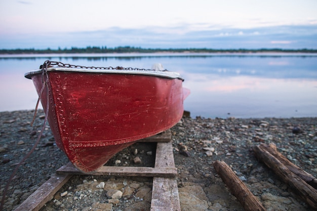 Old red rowboat lying at shore in the evening.