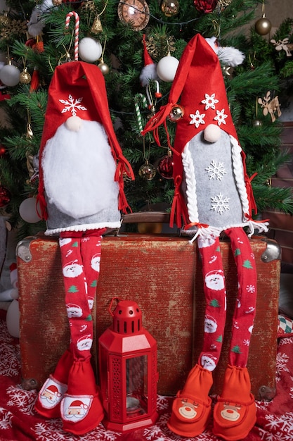 On an old red suitcase sit two New Year's gnomes near a decorated Christmas tree for the holiday