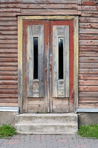 Old red wooden doors entrance to wooden house with withered peeling paint on the walls in in Tartu Estonia