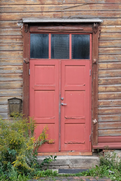 Old red wooden doors entrance to wooden house with withered peeling paint on the walls Tartu Estonia