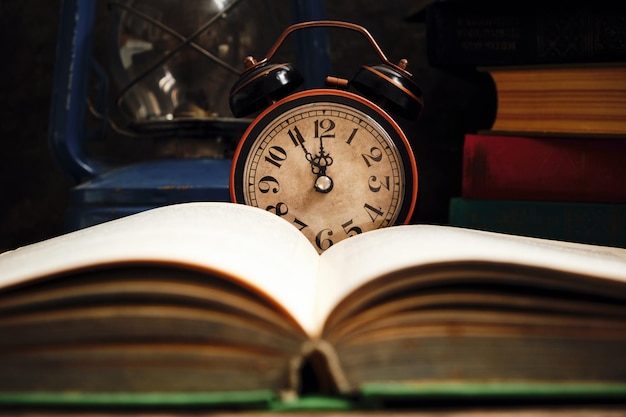 Old retro alarm clock in rustic interior with books and kerosene lamp.Close up.