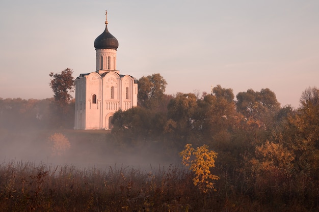 Old Russian Orthodox church lit by the rising sun above autumn forest in a light mist