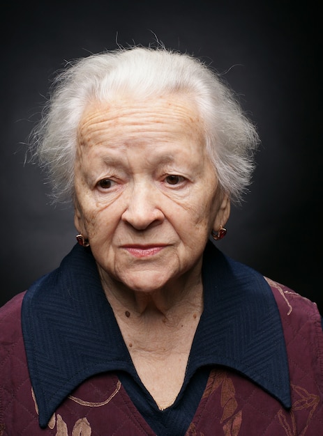 Old sad woman posing in studio over gray background