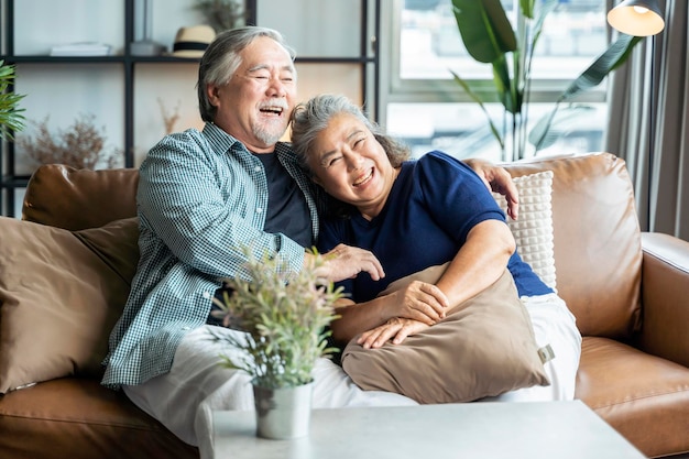 Old senior asian retired age marry ciuple wellness lifesstyle together at homeold people laugh smile together with love and bonding on sofa in living room home interior background