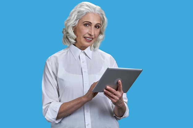 Old senior grayhaired woman with tablet pc isolated on blue background