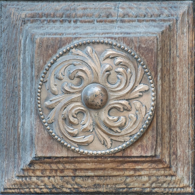 Old shabby bronze circle with a beautiful ornament on a wooden door. Close-up