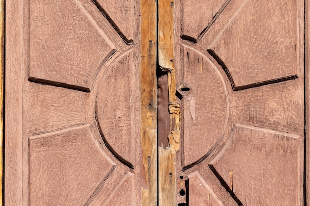 Old shabby wooden door background texture with peeling paint and sun pattern