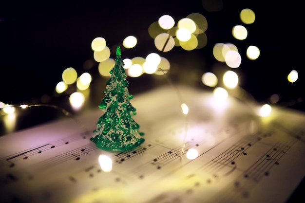 Old sheet with Christmas music notes as background against blurred lights. Christmas music concept