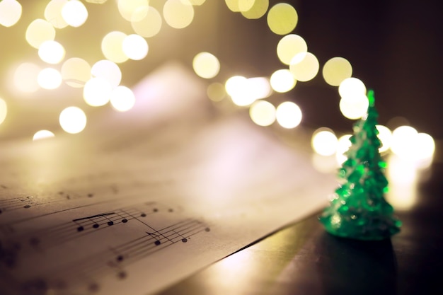 Old sheet with Christmas music notes as background against blurred lights. Christmas music concept