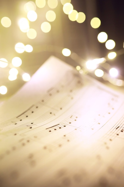 Old sheet with Christmas music notes as background against blurred lights. Christmas music concept