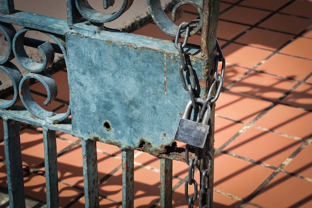 Old steel padlock hanging on chain at rusty metal fence