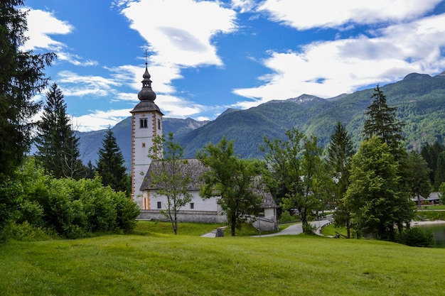 Old stone church on the shore of a mountain lake. Green mountain range and blue sky with white clouds.