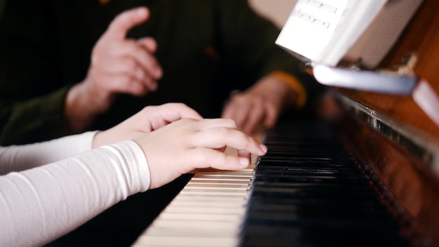 An old teacher teaching little girl how to play piano