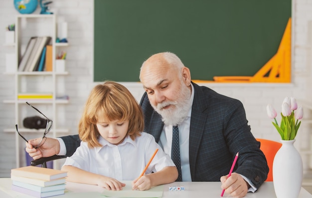 Old teacher and young schoolboy doing homework assignment at school teachers day