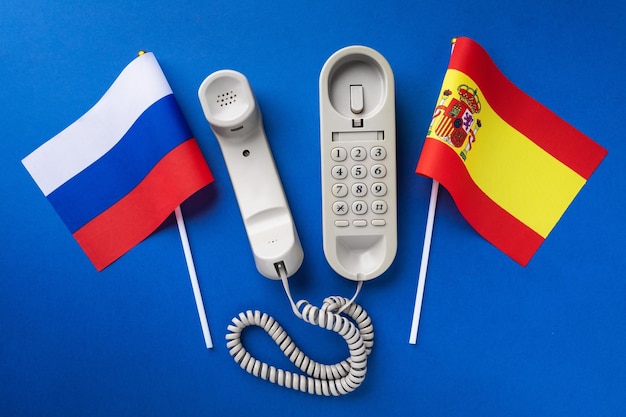 Old telephone and flags of Russia and Spain on a blue background concept