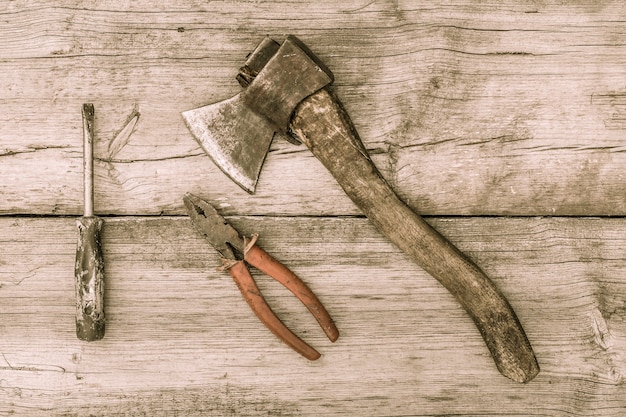 Old tools on wooden background. Old stained axe, pliers and screwdriver on old wooden surface. Vintage style