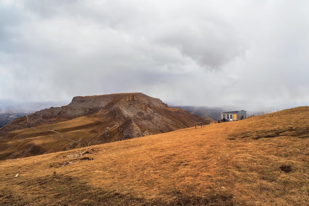 An old tourist wooden house on the edge of a cliff against the backdrop of the majestic autumn plateau of Bermamyt in cloudy weather