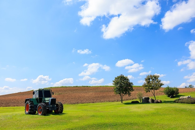 Old tractor in the agriculture farmland on the green grass blue sky background