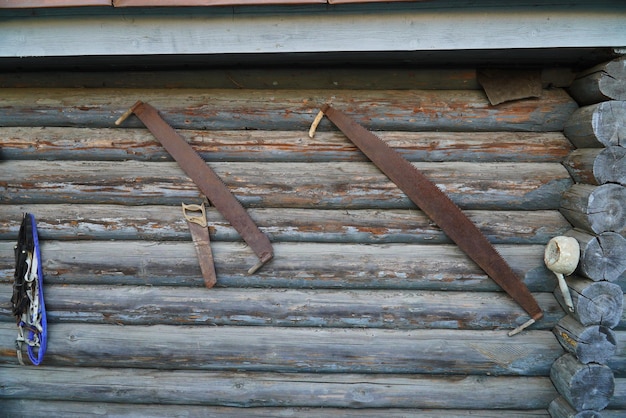 An old twohanded saw is hanging on a wooden wall of logs