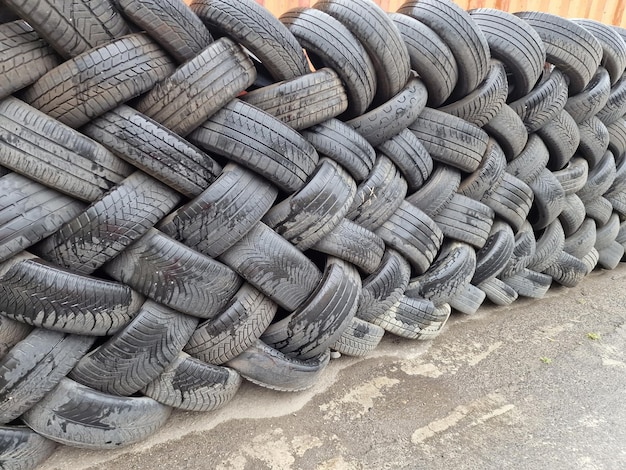 Old used weared car and truck wheels tyres pile stacked in rows stored for recycling Heap of many rubber tires wall background Idustrial pollution of environment