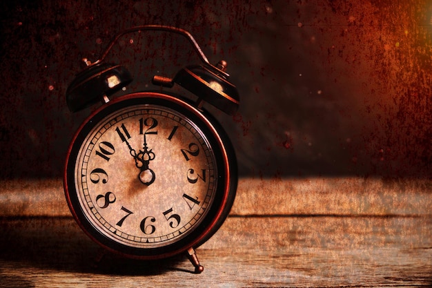 An old vintage alarm clock on a wooden table with dust settling on a background of sunlight.