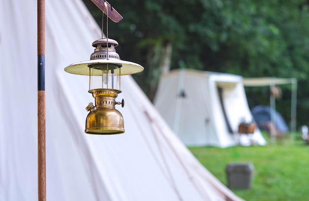 The old vintage camping brass lantern with blurred background of white field tents in camping area