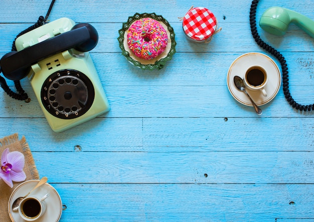 Old vintage telephone, with biscotti, coffee, donuts on a wooden background