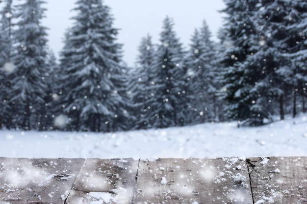 Old vintage wooden table top view with blurry fir tree covered in snow background