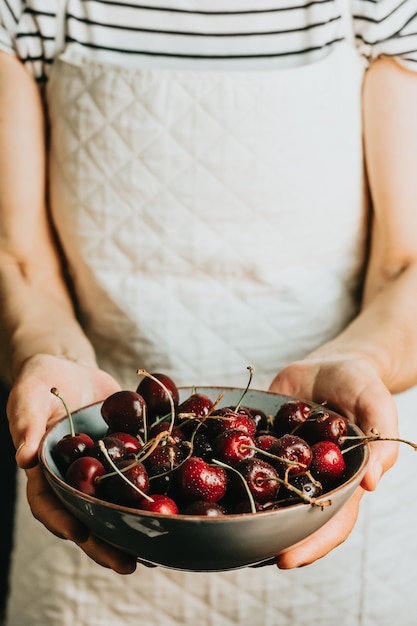 Old waitress offers and holds a bunch of cherry in a dish, fruits, healthy life, good eating, mediterranean concepts, copy space, vertical image