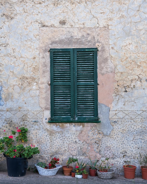 Old wall with green wooden shutters on the window pots of flowers on the ground Mallorca Spain