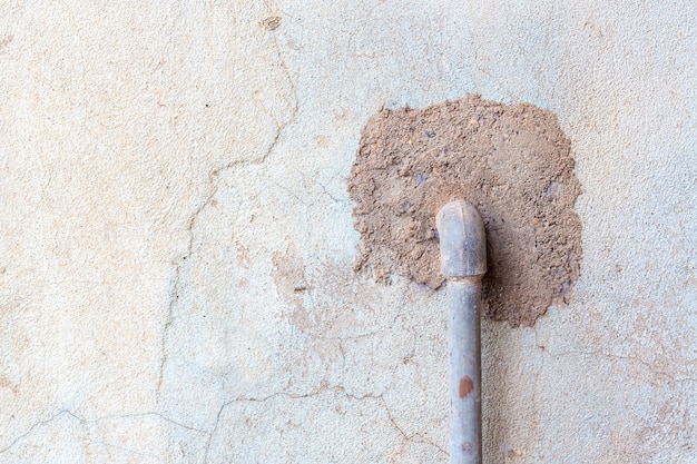 Old, weathered stucco wall with water pipe sticking out of it with cracks 