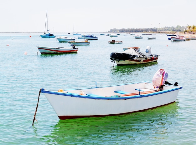 An old white fishing boat and ships in the harbor.