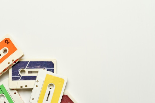 Old white plastic cassette tapes with brightly colored labels stacked in one corner of the image on a white background