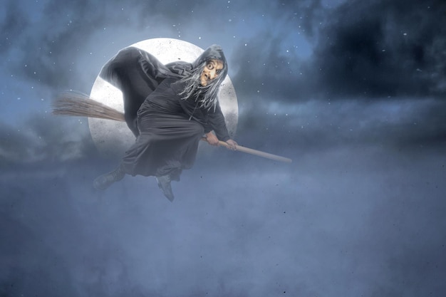 Old witch in a cloak flying on a broomstick in the night