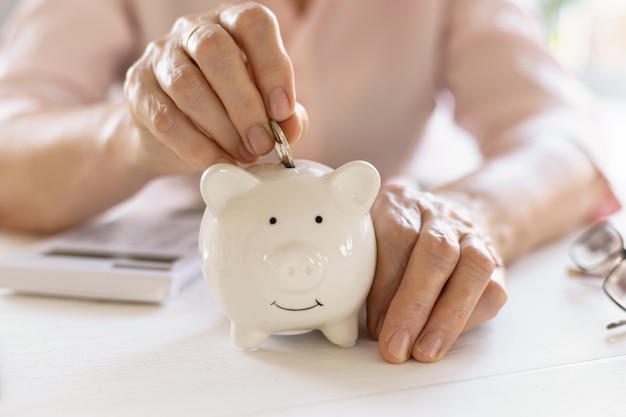 Old woman hands put money coins in a piggy