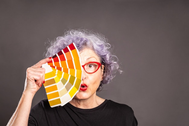 Photo old woman holding a color palette on a gray space