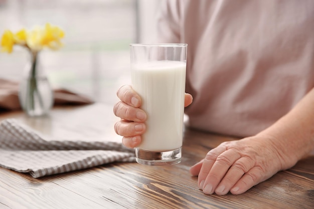 Old woman holding glass with fresh milk over table