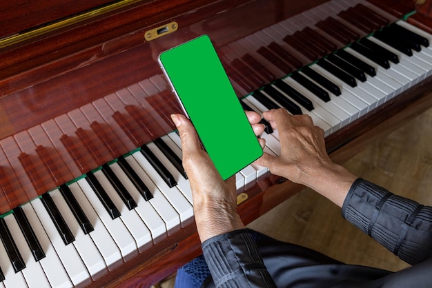 Old woman plays the piano looks into the phone notes Chroma key on smartphone