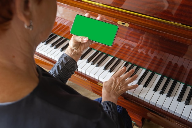 Old woman plays the piano looks into the phone notes Chroma key on smartphone