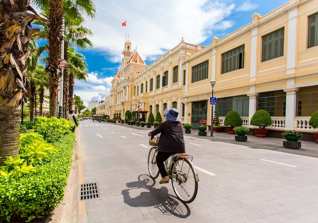 Old woman ridding bicycle on the road in the front of Ho Chi Minh City Hall