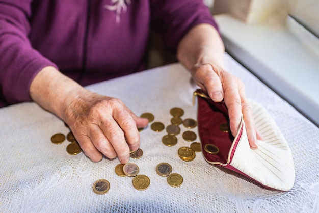 Old woman sitting miserably at home and counting remaining coins from the pension