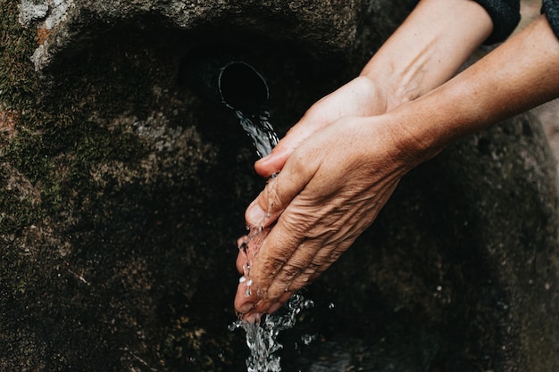 An old woman washing her hands close up of the hands in a source font with natural water