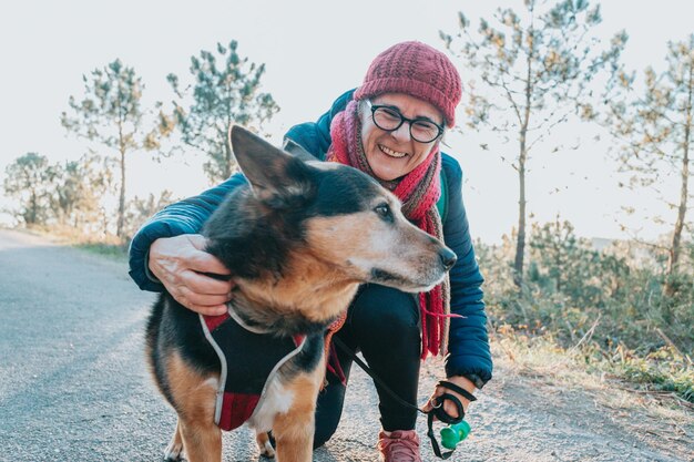 Old woman with his dog during a walk portrait wearing a hat for spring and winter smiling toc amera Senior people mental health activities outdoors Active lifestyle on third age Happy grandma