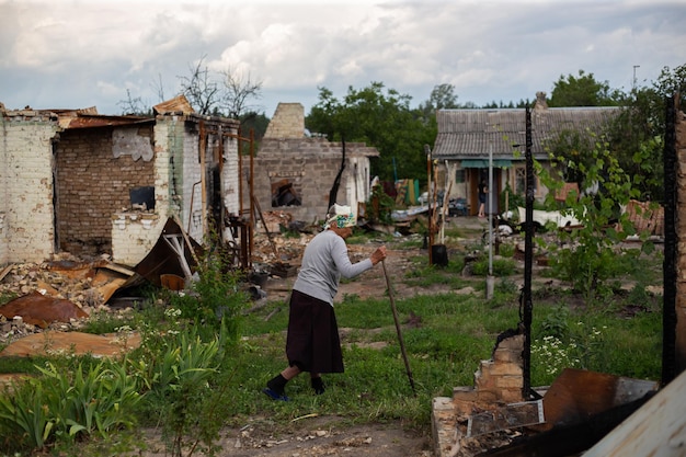 An old woman with a stick on the background of a destroyed house during the Russian invasion of Ukraine