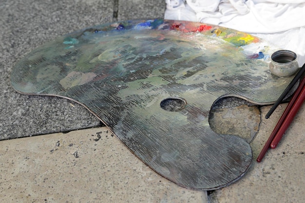 Old wooden art palette with oil paints and a brushes on the floor