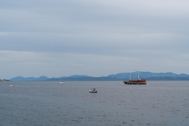 An old wooden boat with many tourists on board in the Adriatic Sea It's evening High mountains on the horizon Small yachts and boats sail nearby Croatia